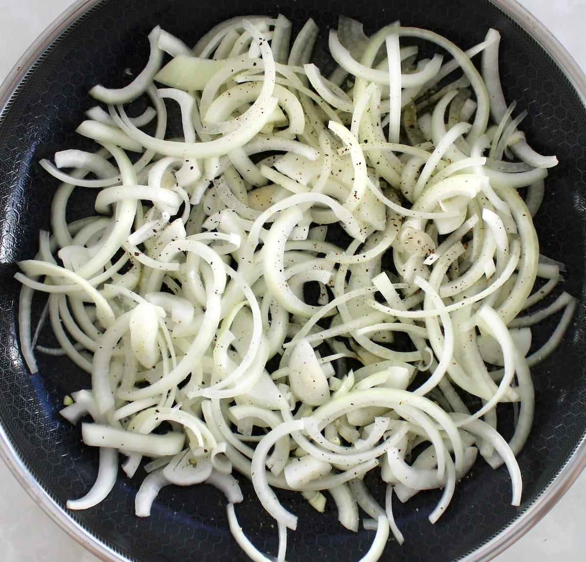 sliced onions in skillet with salt and pepper