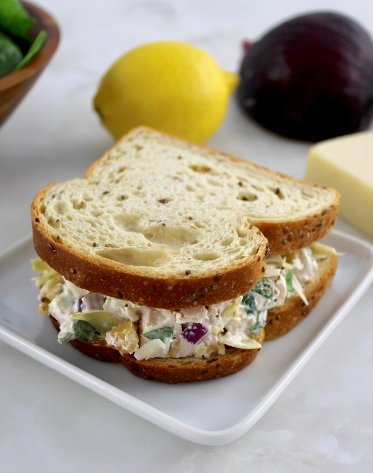 Spinach Artichoke Chicken Salad sandwich on sola bread on white plate