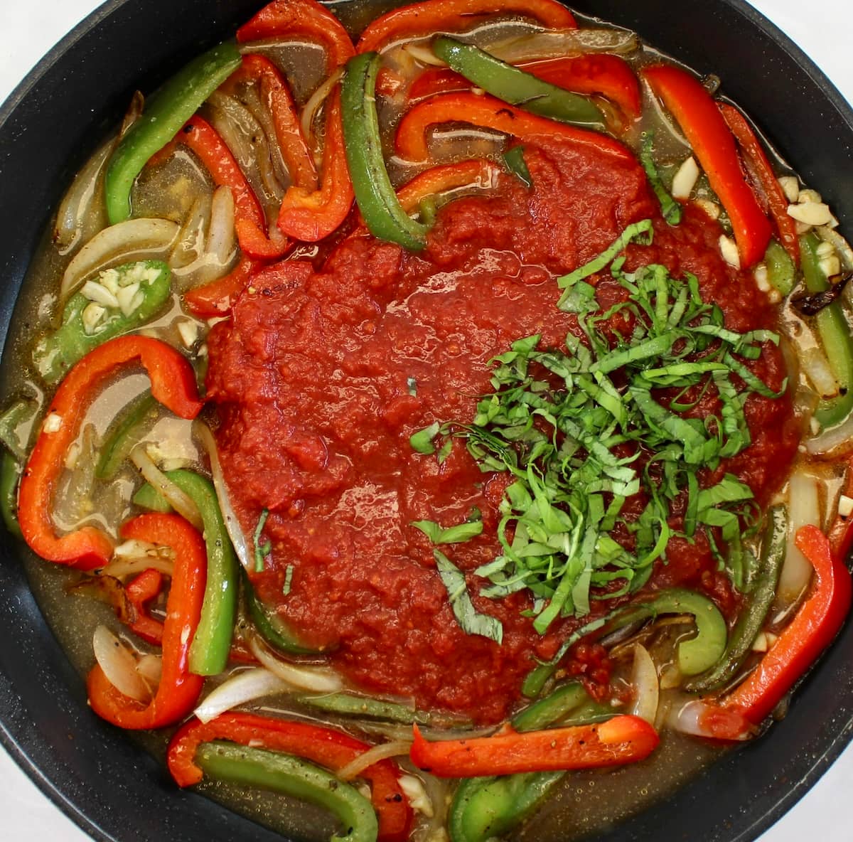bell peppers and onions with crushed tomatoes and sliced basil in skillet