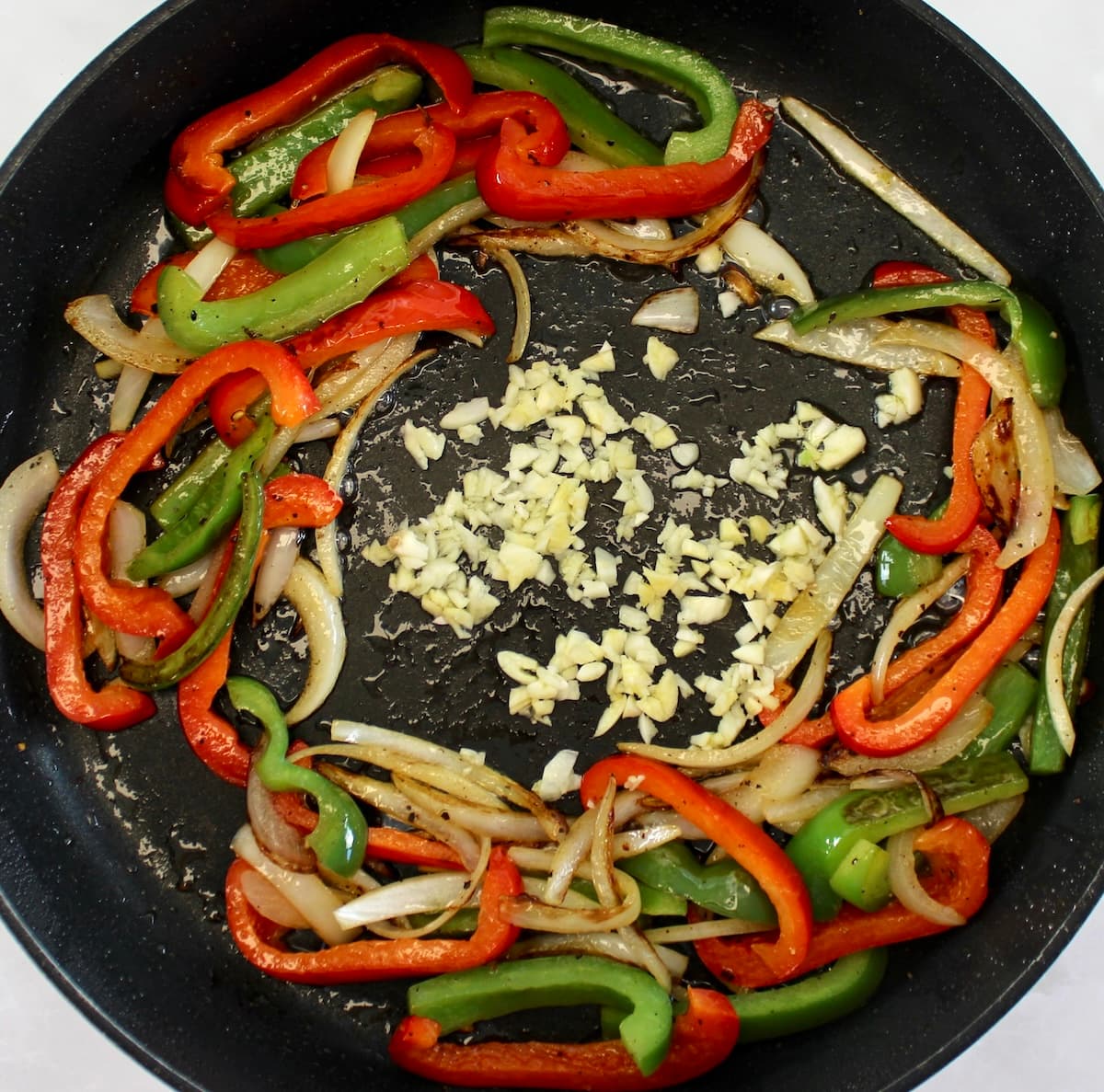 red and green bell pepper, garlic and onion slices cooking in skillet