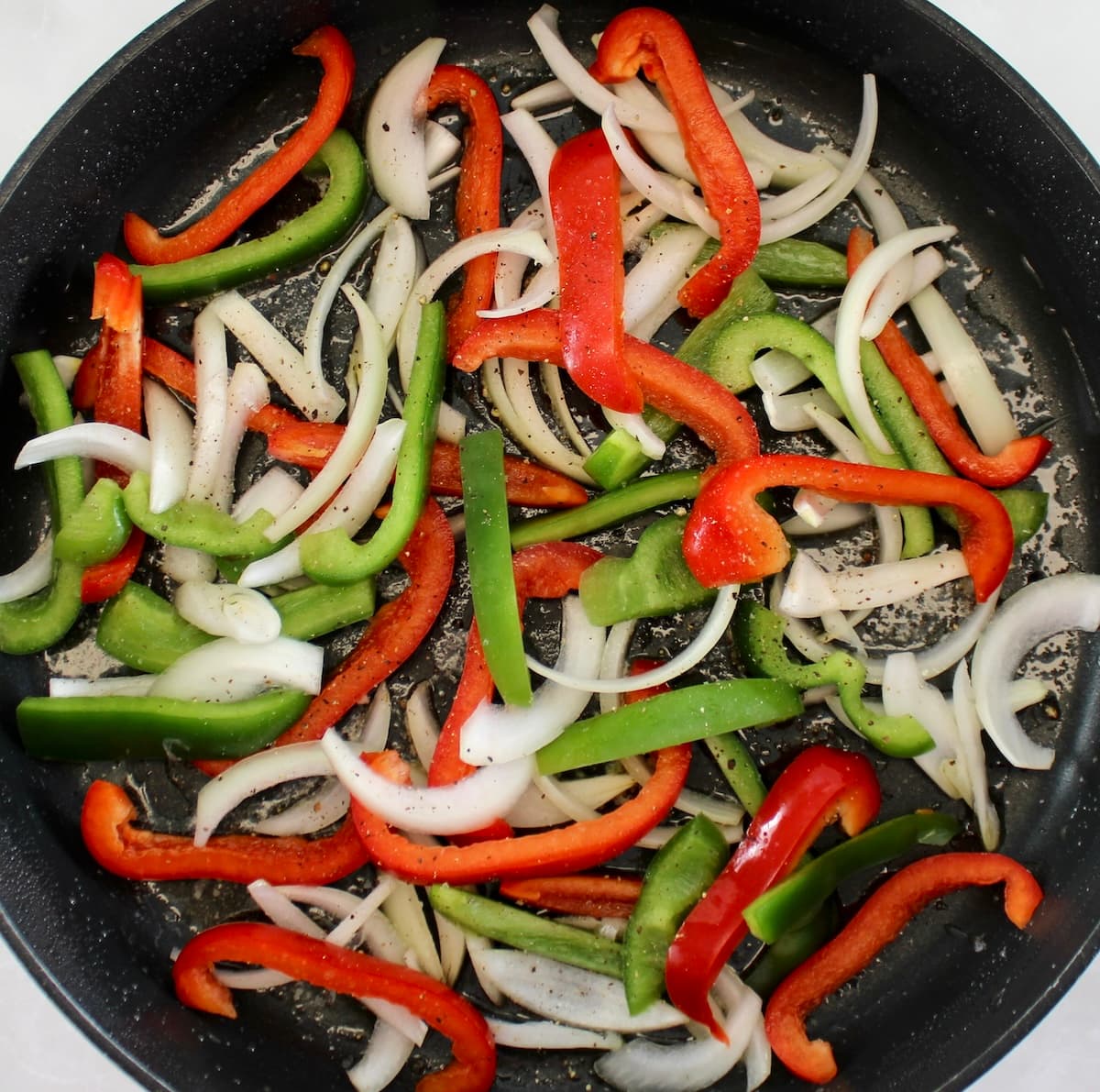 red and green bell pepper and onion slices cooking in skillet