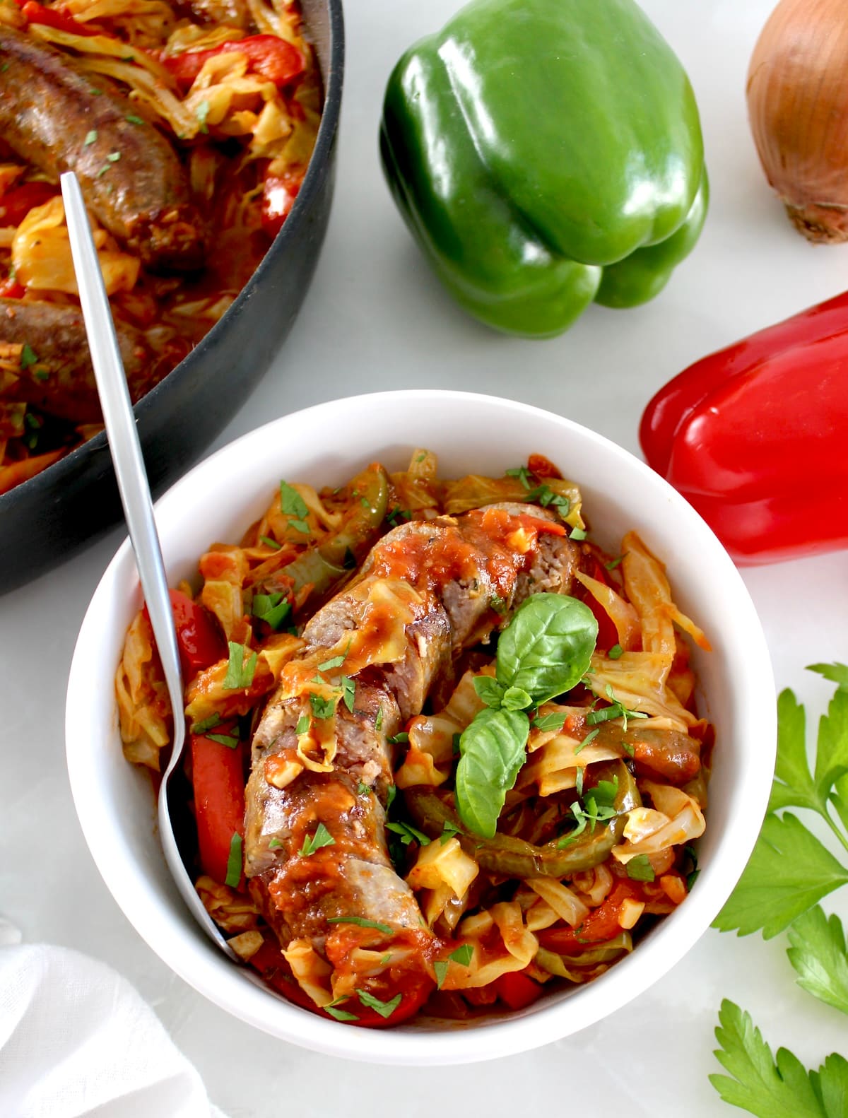 Italian Sausage and Peppers Cabbage Skillet in white bowl with spoon and sausage link sliced