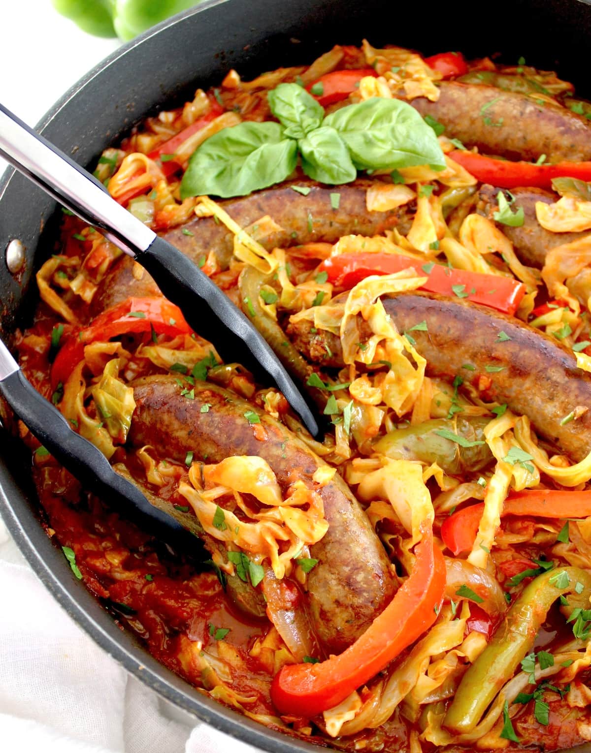 closeup of Italian Sausage and Peppers Cabbage Skillet in skillet with black tongs
