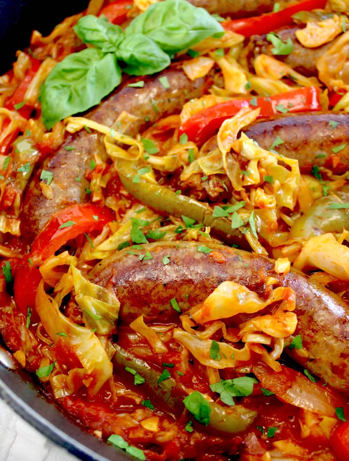 closeup of Italian Sausage and Peppers Cabbage Skillet in skillet with fresh basil garnish