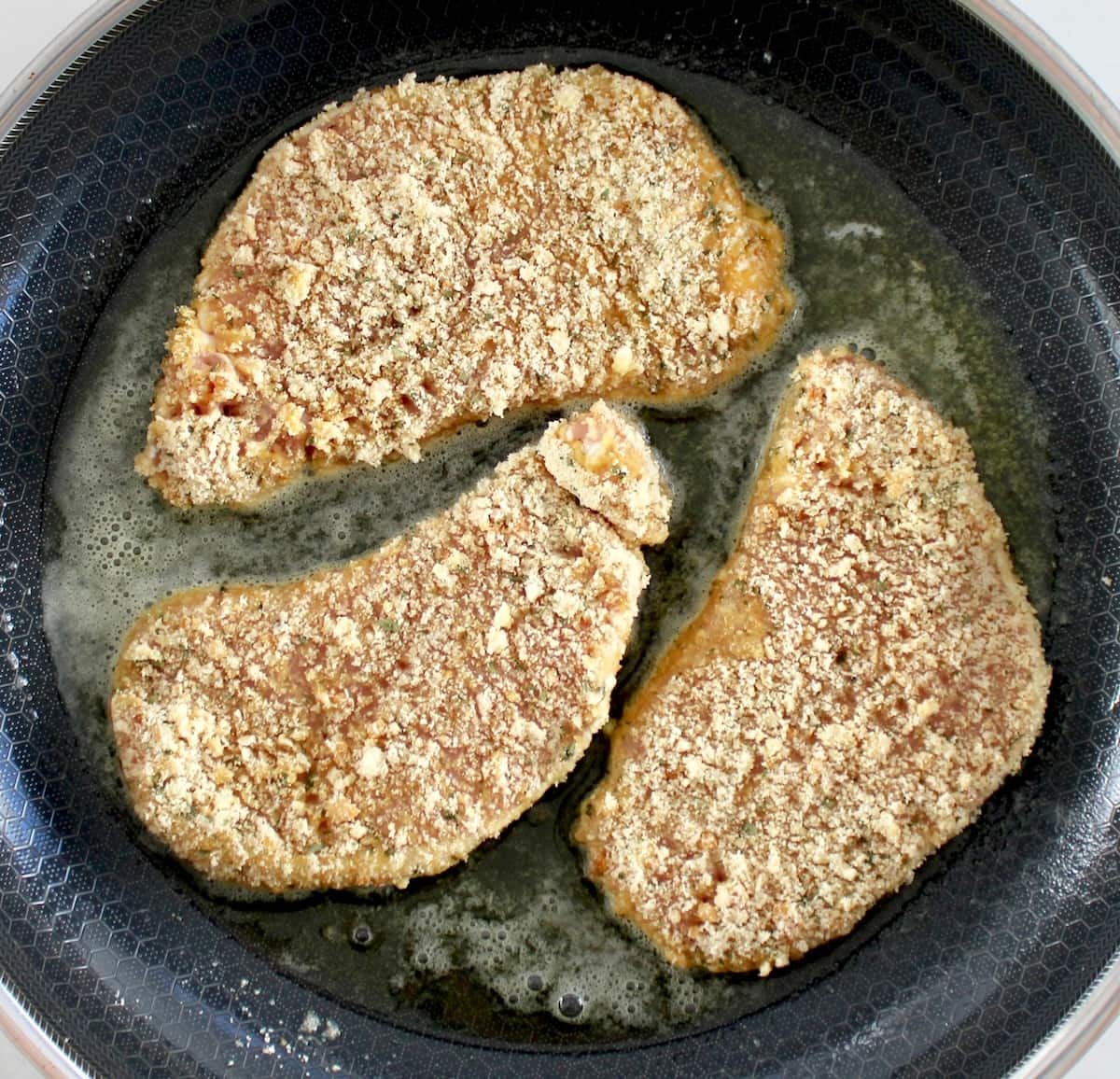 3 Pork Milanese chops frying in skillet
