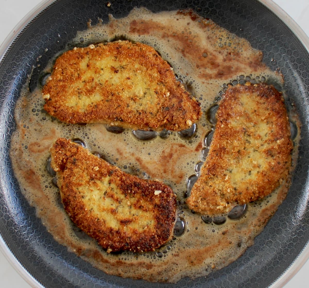 3 Pork Milanese chops frying in skillet