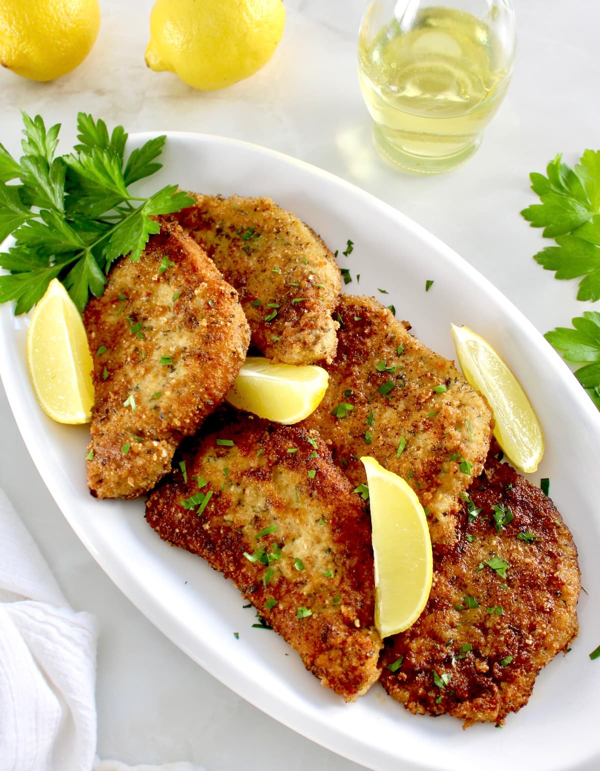 Pork Milanese on white oval platter with lemon wedges and fresh parsley