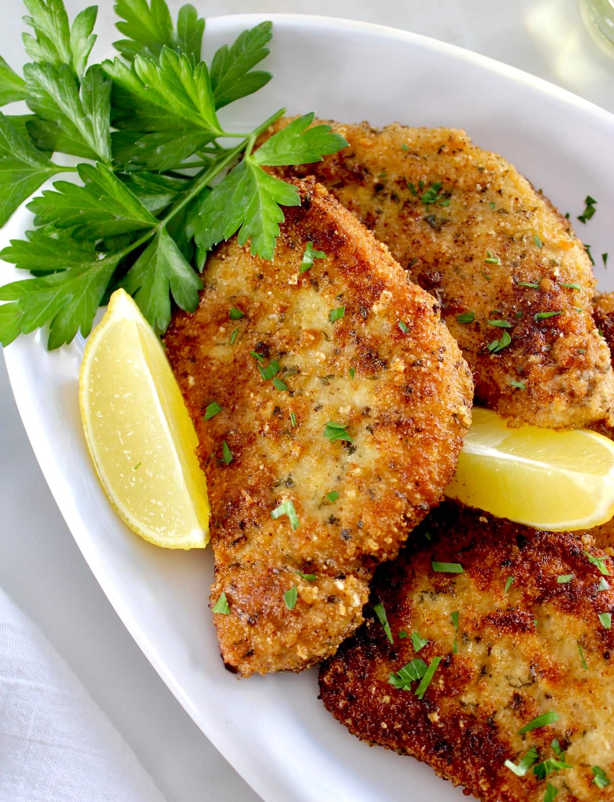 closeup of Pork Milanese on white platter with lemon wedges and parsley