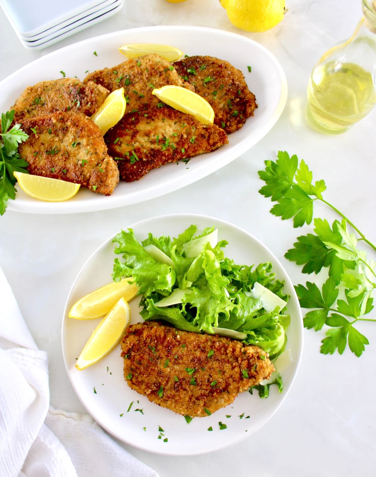 overhead view of Pork Milanese on white plate with greens and more chops on white platter in back