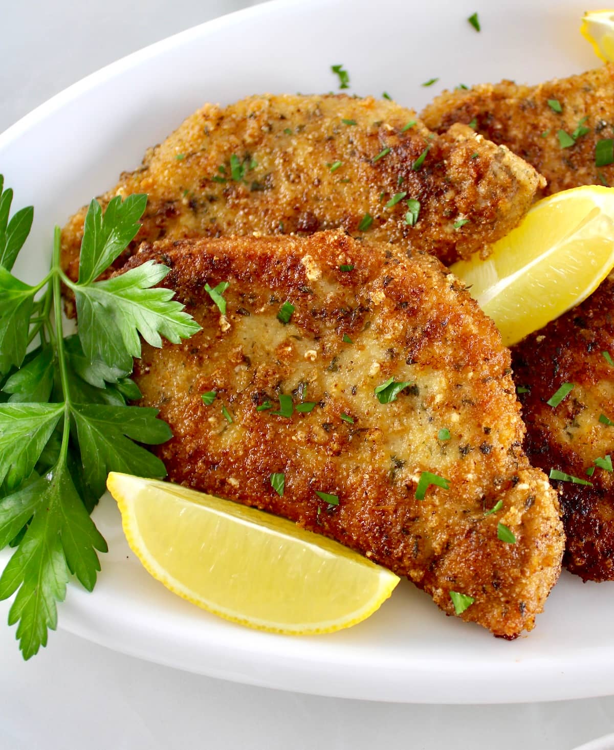 closeup of Pork Milanese on white plate with lemon wedges and parsley
