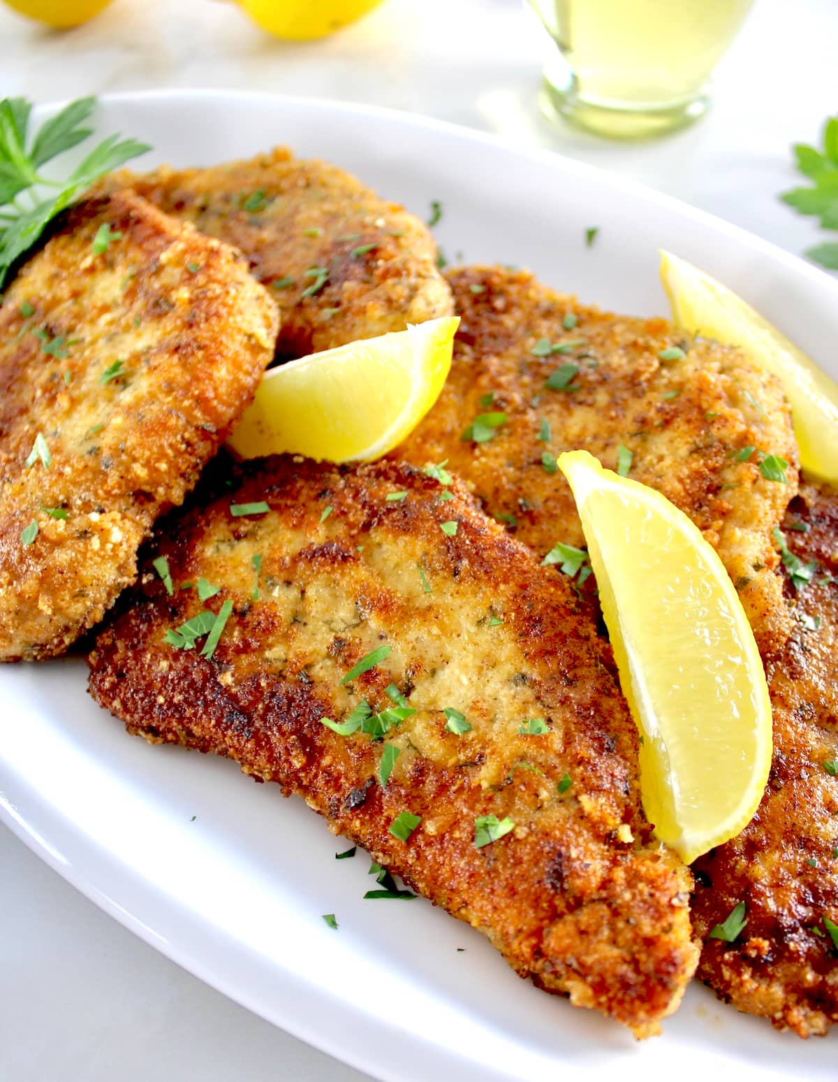 closeup of Pork Milanese on white plate with lemon wedges and parsley