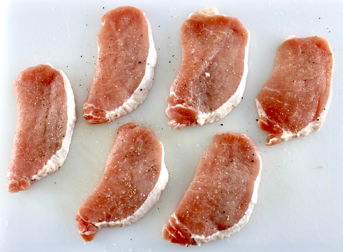 6 raw pork chops on cutting board with salt and pepper
