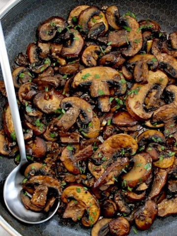 Sautéed Mushrooms in skillet with silver serving spoon on side