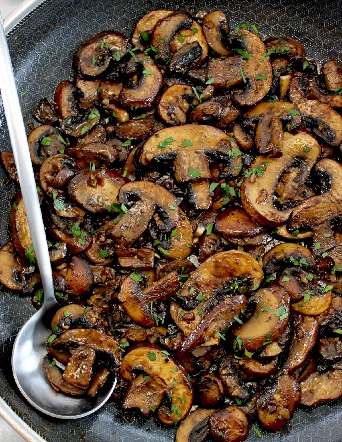 Sautéed Mushrooms in skillet with silver serving spoon on side