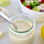 Lemon Tahini Dressing in open glass jar with spoon and salad in back