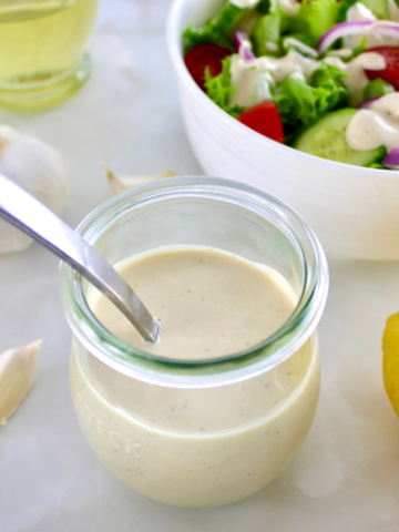 Lemon Tahini Dressing in open glass jar with spoon and salad in back