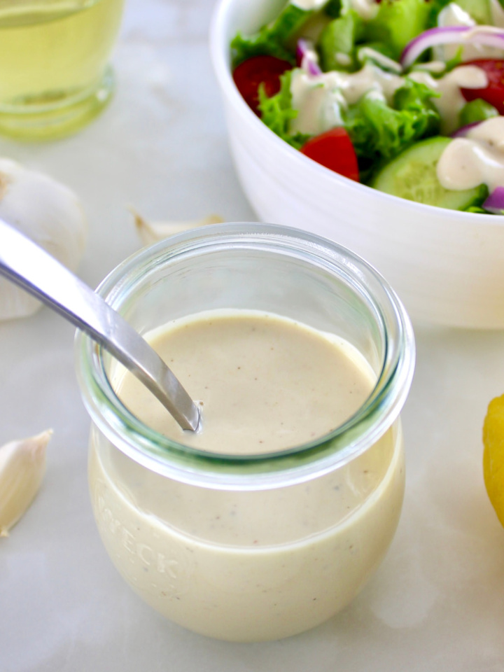 Lemon Tahini Dressing in open glass jar with spoon and salad in back