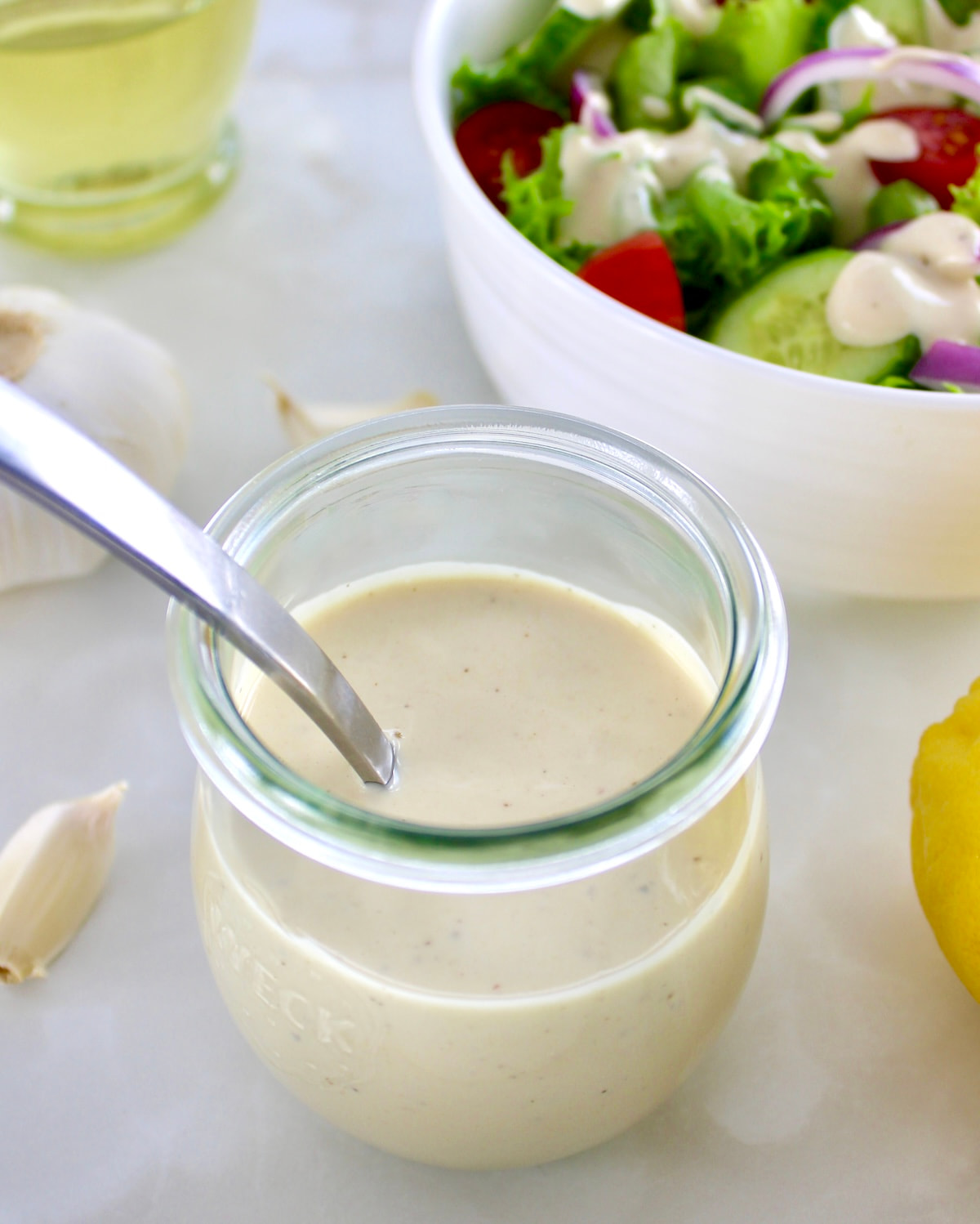 Lemon Tahini Dressing in open glass jar with spoon and salad in back