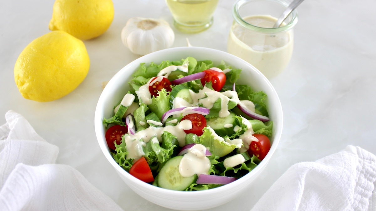 Lemon Tahini Dressing over salad with lemons, garlic and more dressing in back