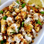 Roasted Cauliflower with Tahini on white plate with fresh mint and lemon slices