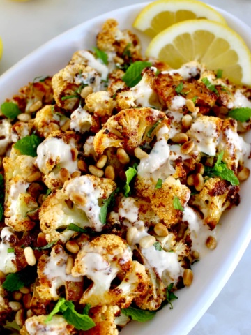 Roasted Cauliflower with Tahini on white plate with fresh mint and lemon slices