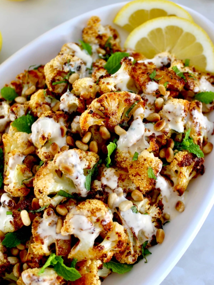 Roasted Cauliflower with Tahini on white plate with fresh mint and lemon slices