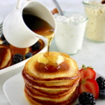 Cottage Cheese Pancakes on plate with berries and maple syrup pouring over top