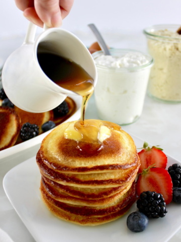 Cottage Cheese Pancakes on plate with berries and maple syrup pouring over top