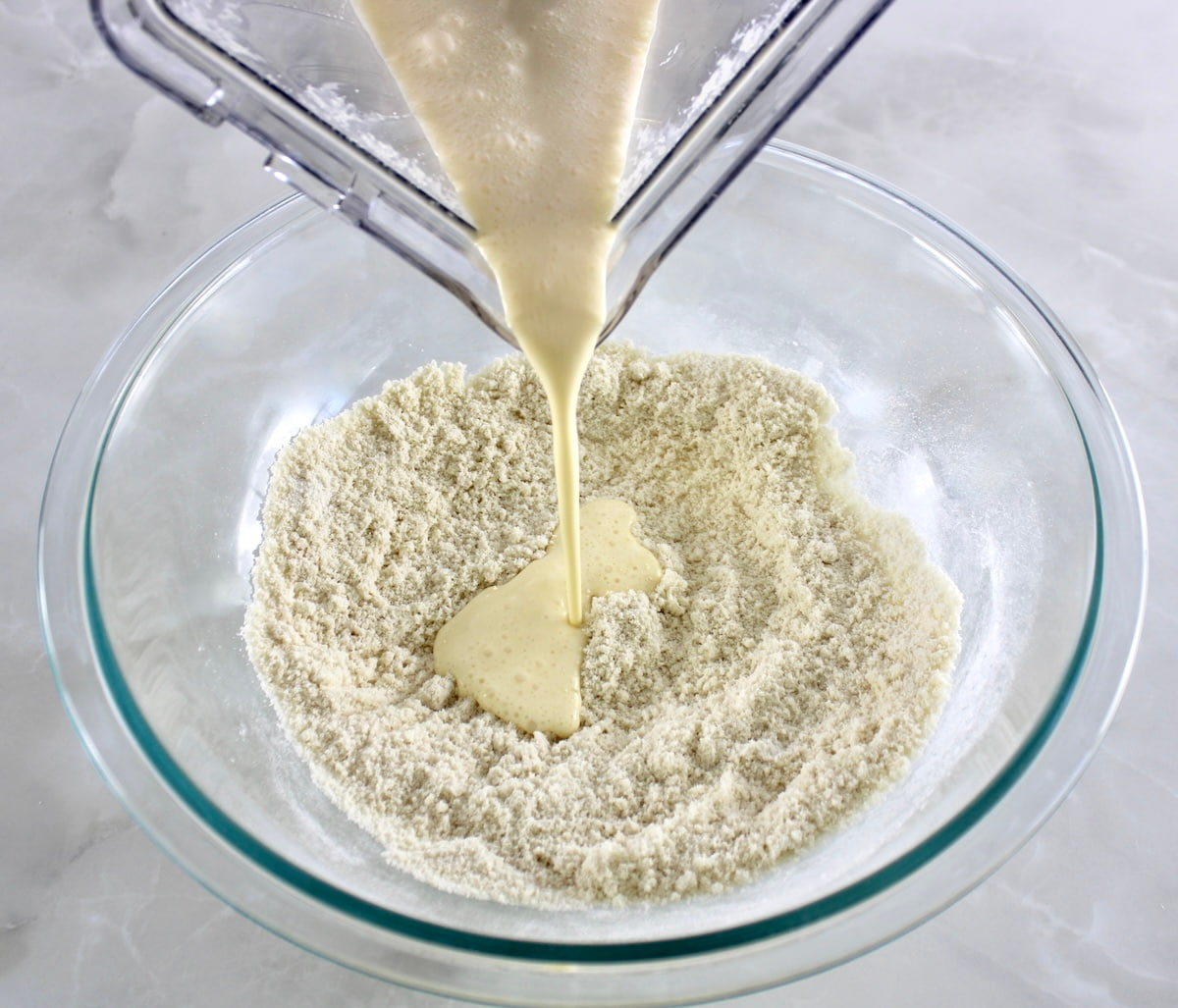 wet ingredients for Cottage Cheese Pancakes pouring into the dry in glass bowl