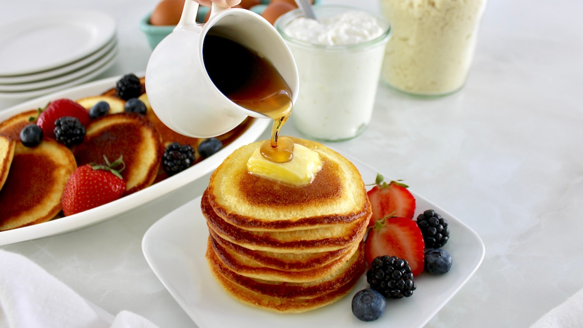 Cottage Cheese Pancakes on plate with berries and maple syrup pouring over top