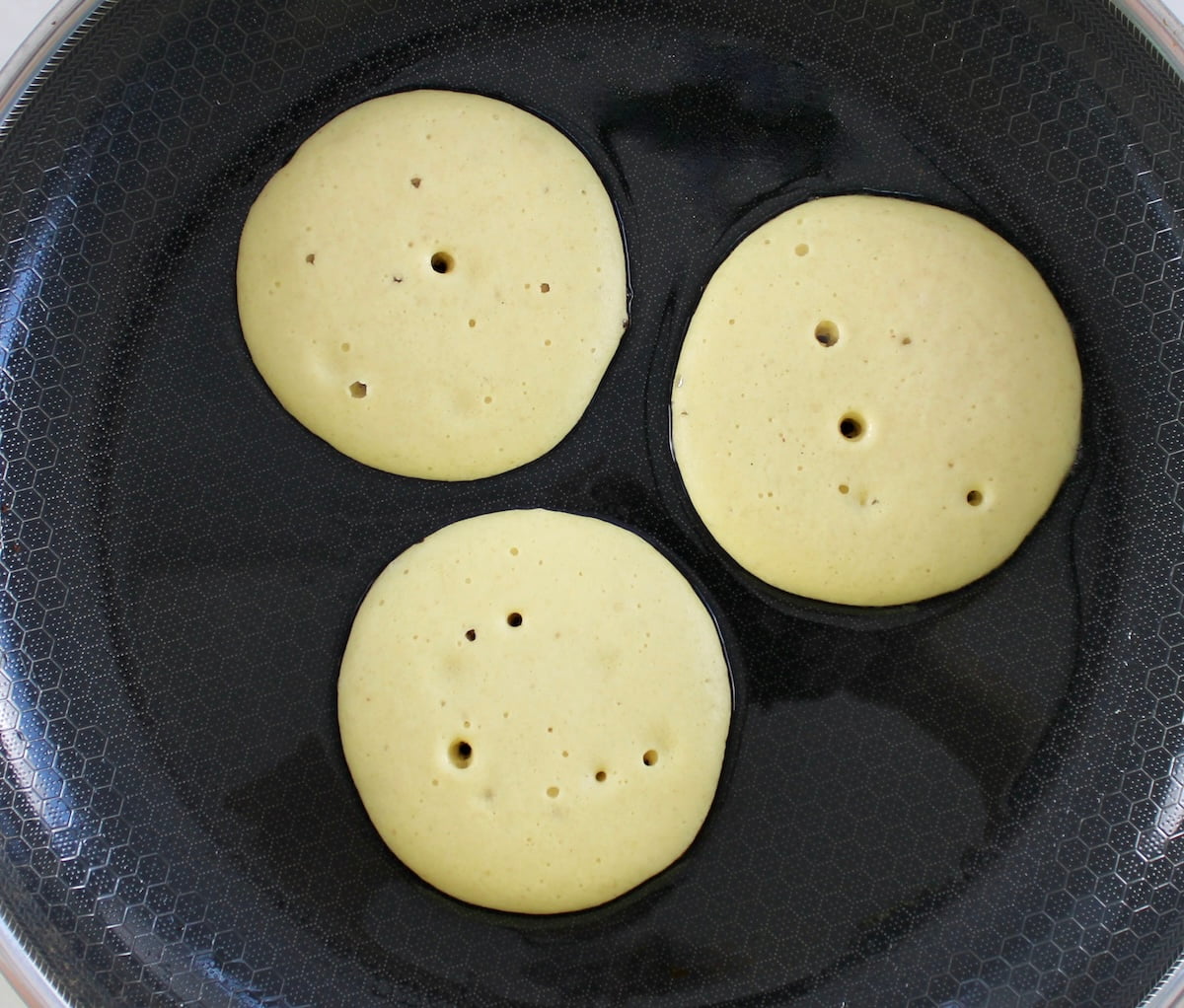 3 Cottage Cheese Pancakes cooking in skillet with tiny bubbles