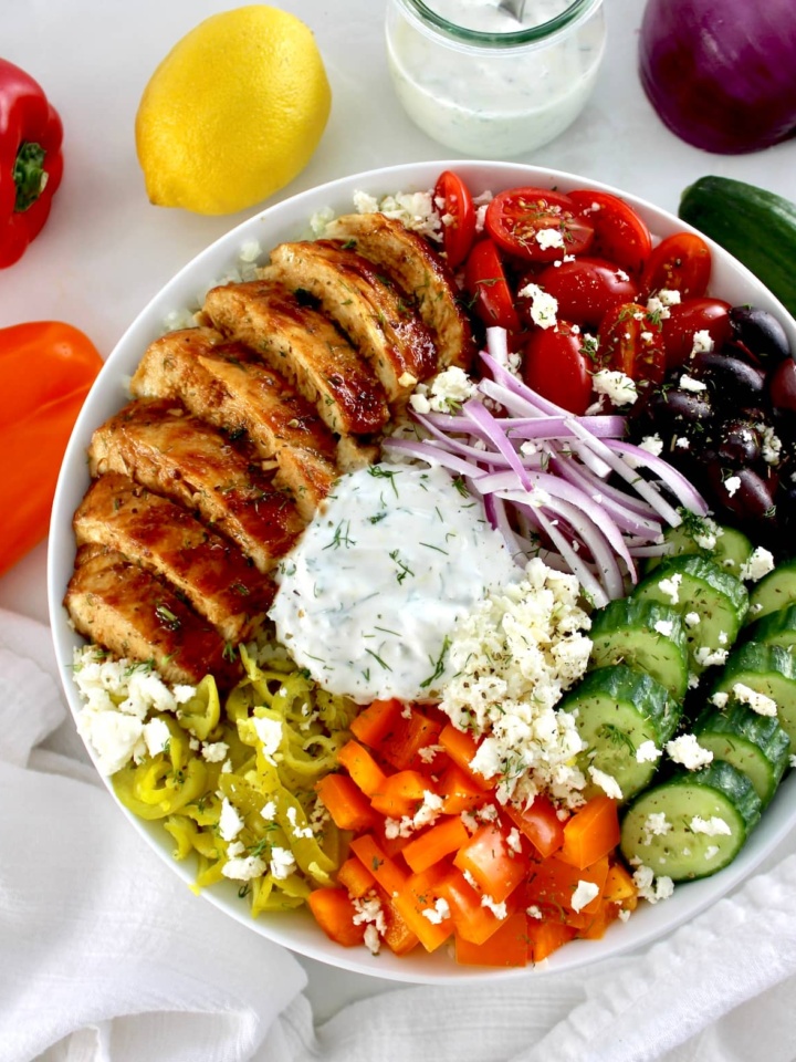 overhead view of Greek Chicken Bowl with lemon and peppers in back