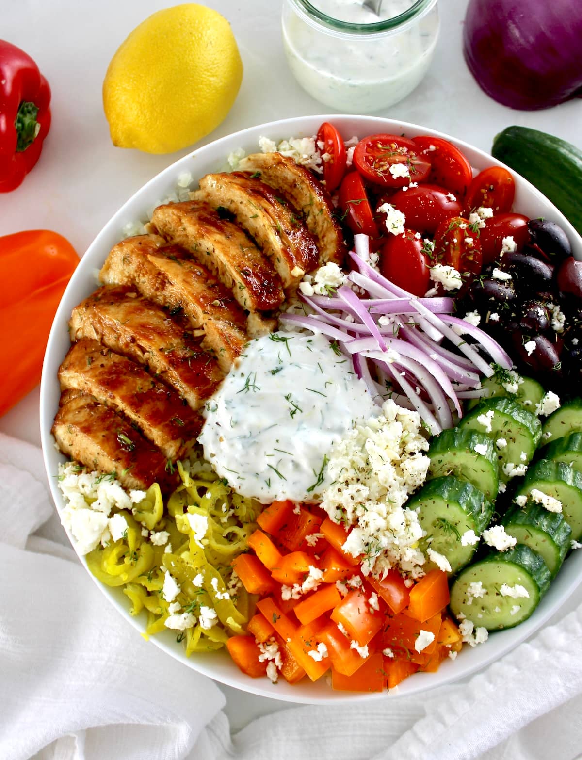 overhead view of Greek Chicken Bowl with lemon and peppers in back
