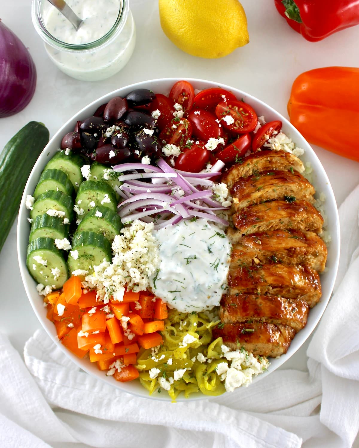overhead view of Greek Chicken Bowl with veggies and sauce in back