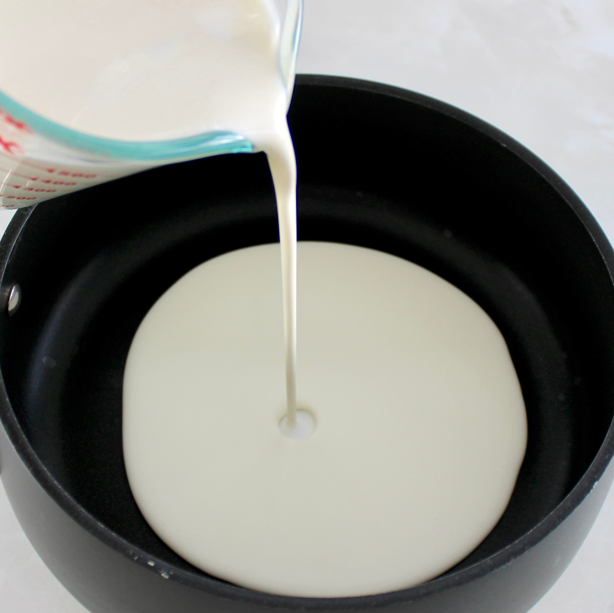 pouring heavy cream into saucepan