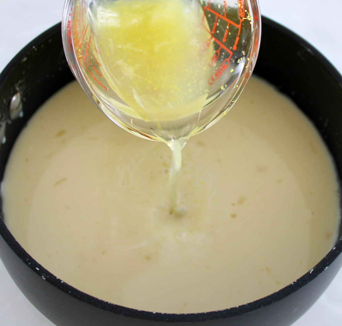 lemon juice being poured into heavy cream in saucepan