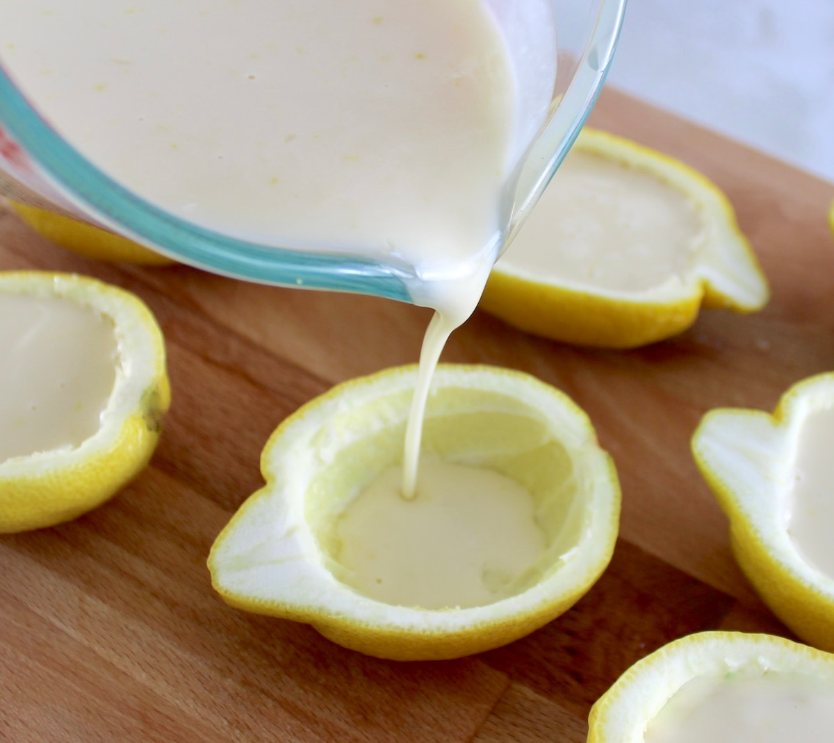 Lemon Posset pouring into scooped out lemon halves on cutting board
