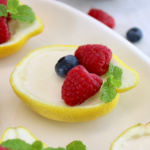 closeup of Lemon Posset in lemon half on white plate with fresh berries and mint on top