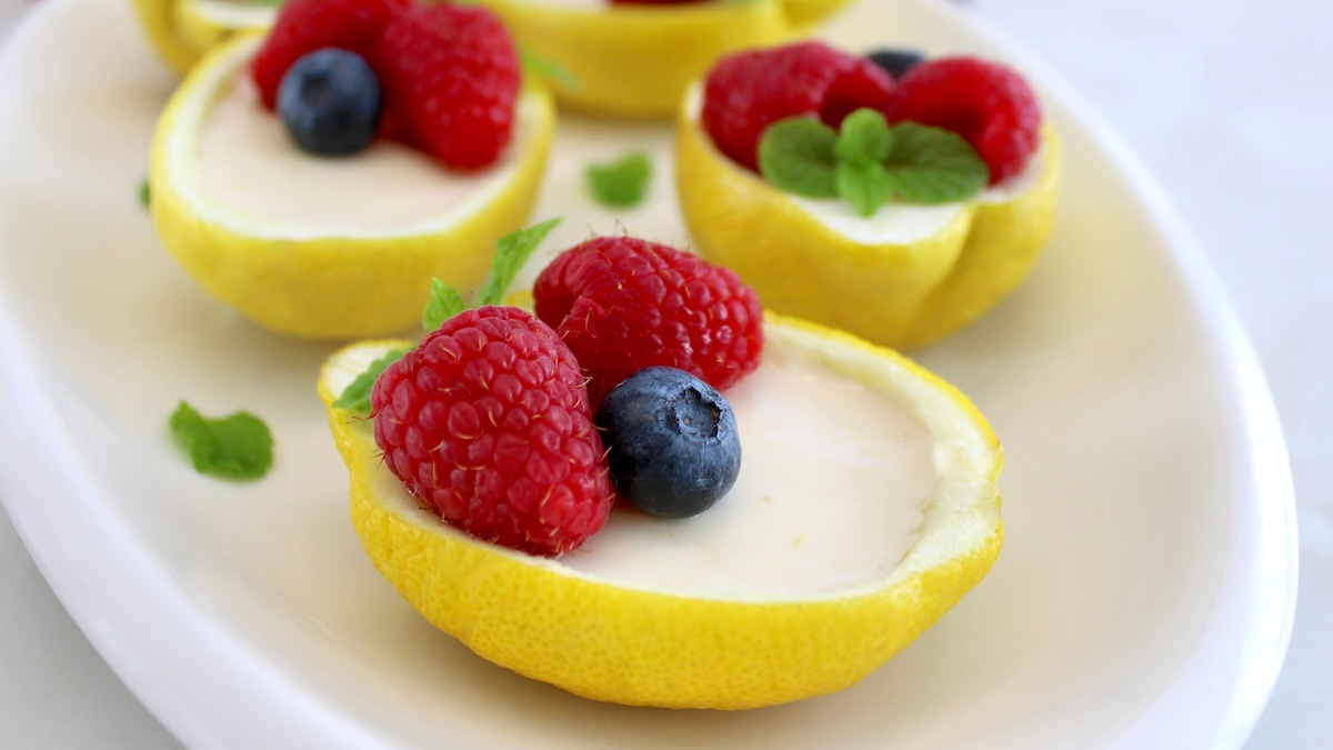 Lemon Posset in lemon halves on white plate with berries on top