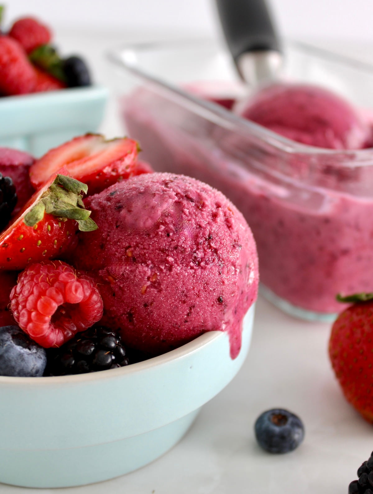 side view of Mixed Berry Frozen Yogurt in blue bowl with fresh berries on top