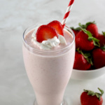 Strawberry Protein Shake in glass with striped straw, whip cream and strawberry slices on top