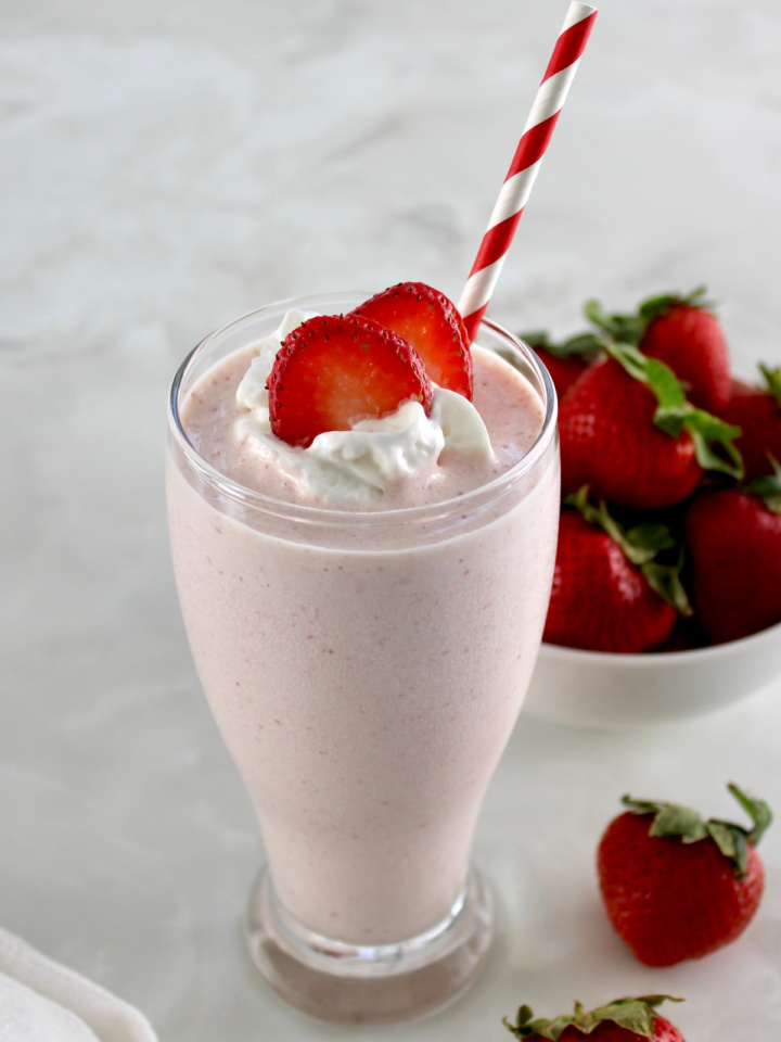Strawberry Protein Shake in glass with striped straw, whip cream and strawberry slices on top