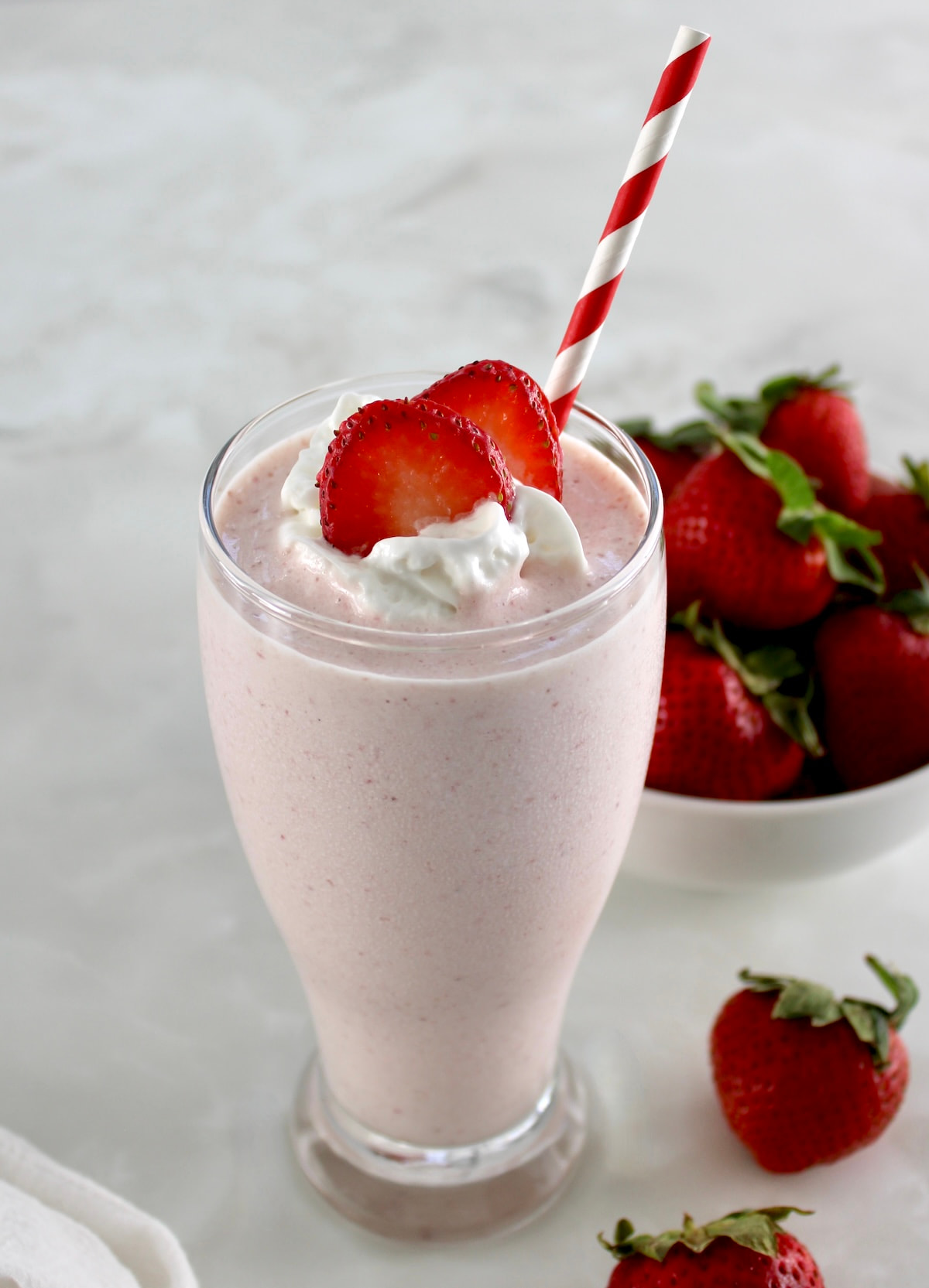 Strawberry Protein Shake in glass with striped straw, whip cream and strawberry slices on top