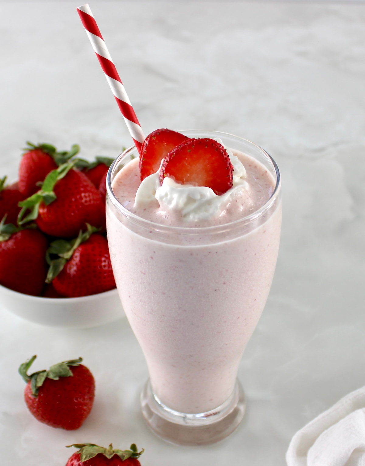 side view of Strawberry Protein Shake in glass with whip cream and strawberry slices on top