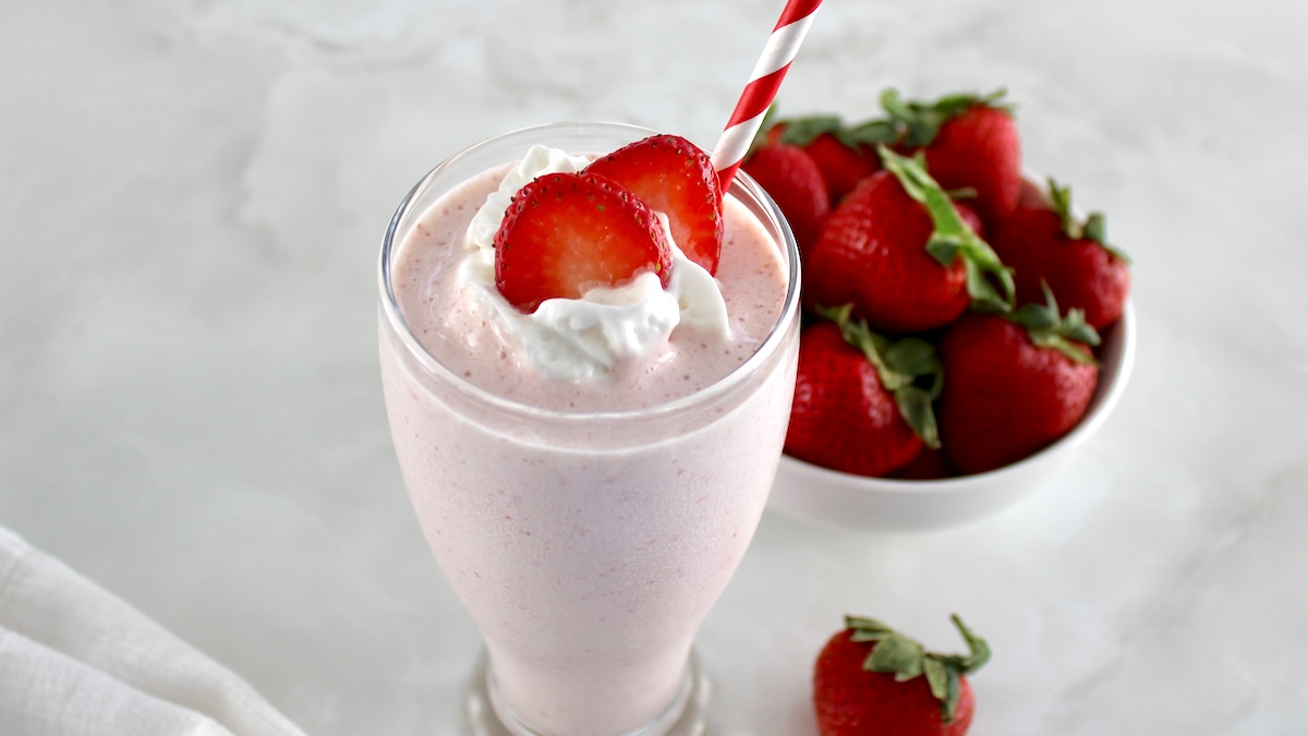 side view of Strawberry Protein Shake in glass with strawberry slices and whip cream on top