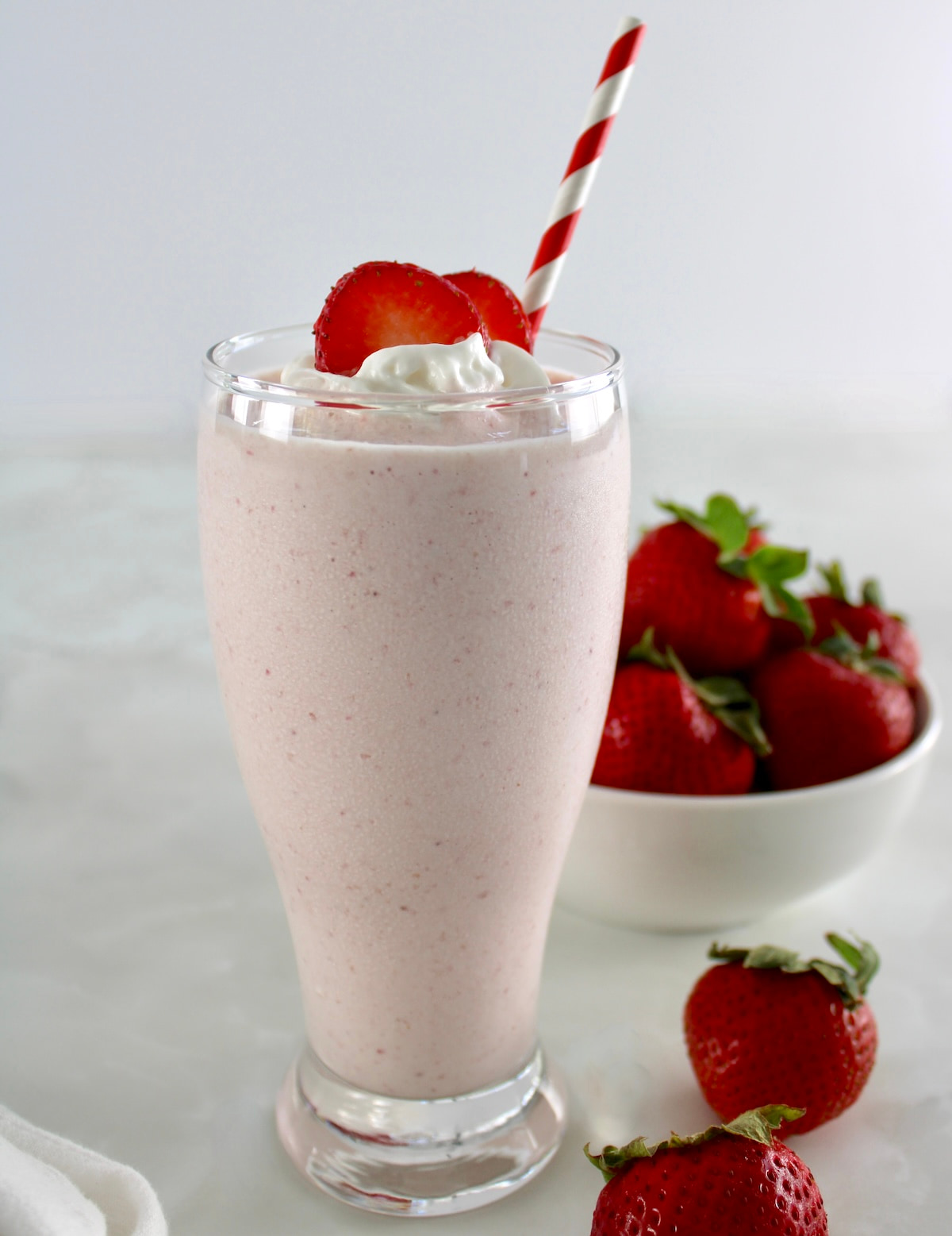 side view of Strawberry Protein Shake with straw, strawberries and whip cream on top
