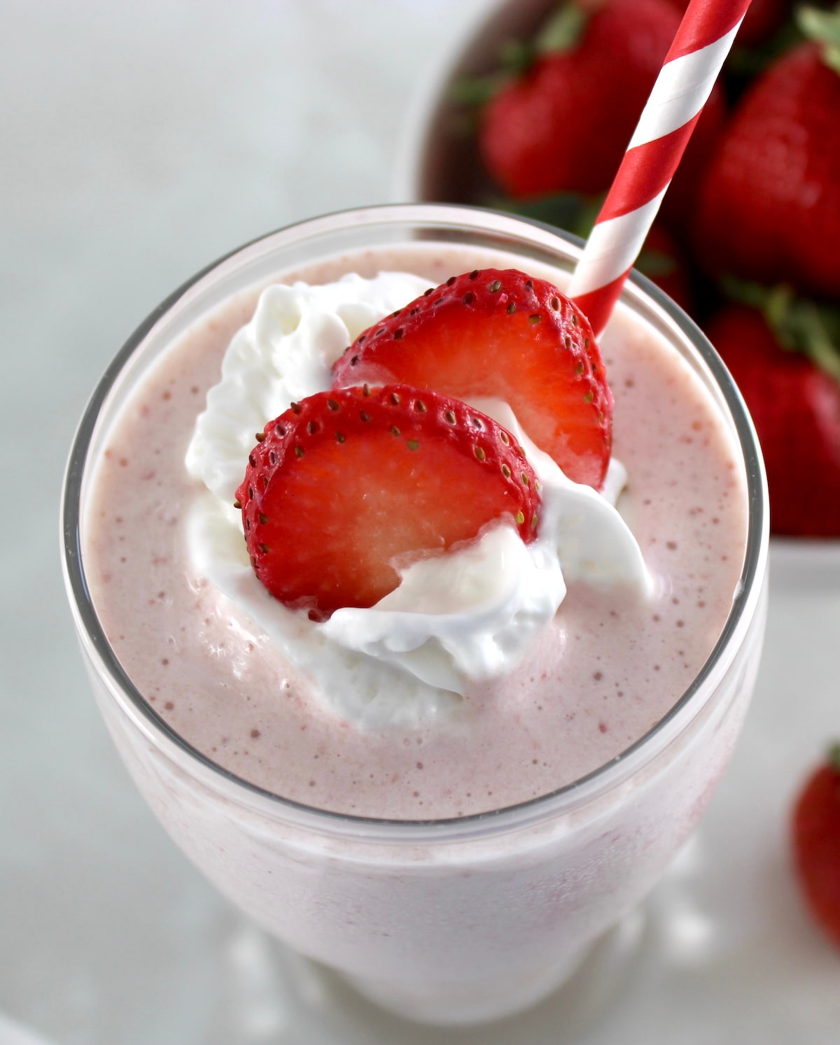 closeup overhead view of Strawberry Protein Shake with strawberry slices and whip cream on top with red and white straw