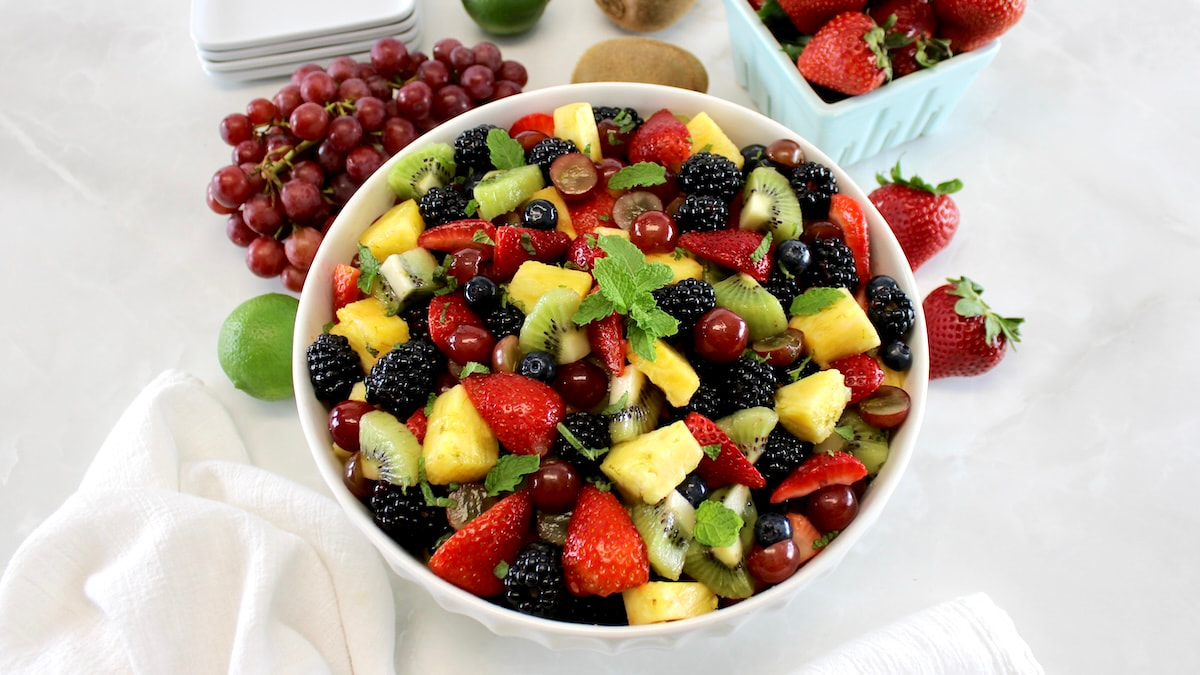overhead view of Easy Fruit Salad in white bowl with more fresh fruit in back