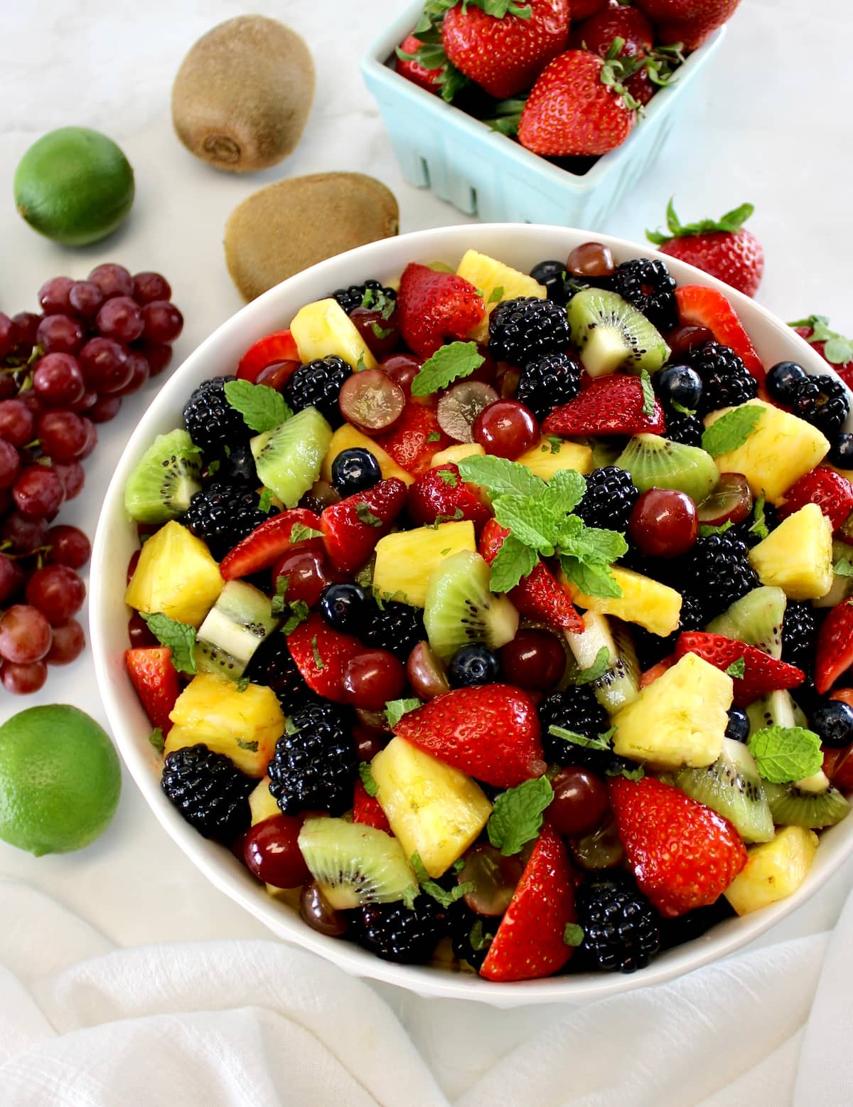 overhead view of Easy Fruit Salad in white bowl with fresh fruit in back