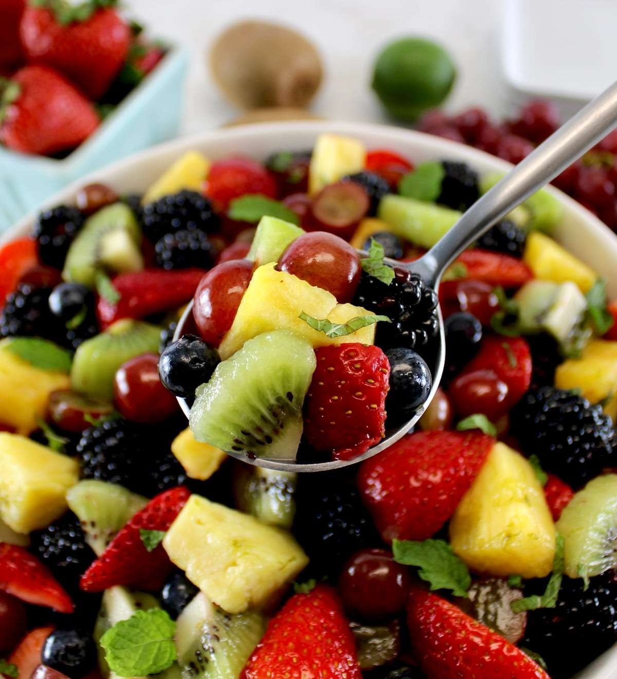 holding up spoonful of Easy Fruit Salad over salad in white bowl